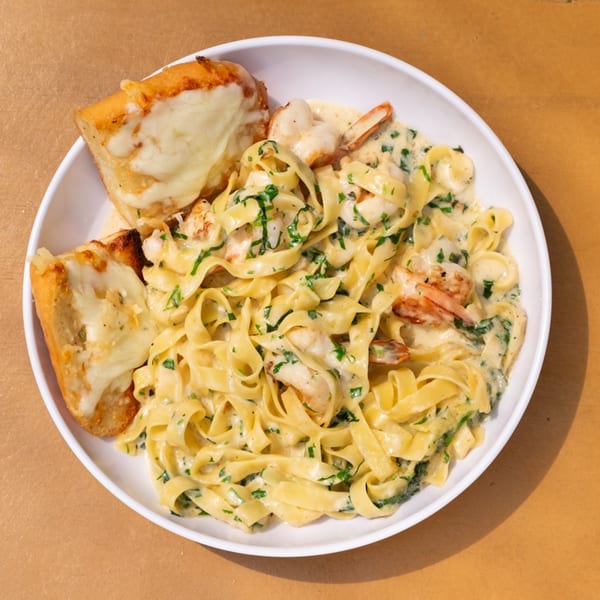Creamy shrimp fettuccine pasta with fresh parsley and two slices of cheesy garlic bread.