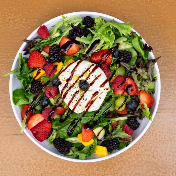A vibrant Tardino Brother's Italian salad with mixed greens, berries, mango, and burrata cheese drizzled with balsamic glaze.