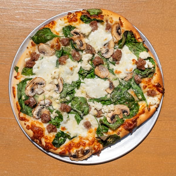 A Tardino Brother's white pizza with spinach, mushrooms, and sausage on a metal pan.