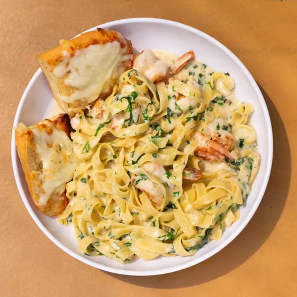 Creamy shrimp fettuccine pasta with parsley and two slices of cheesy garlic bread in a white bowl.