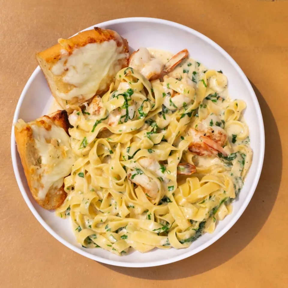 Creamy shrimp fettuccine pasta with parsley and two slices of cheesy garlic bread in a white bowl.