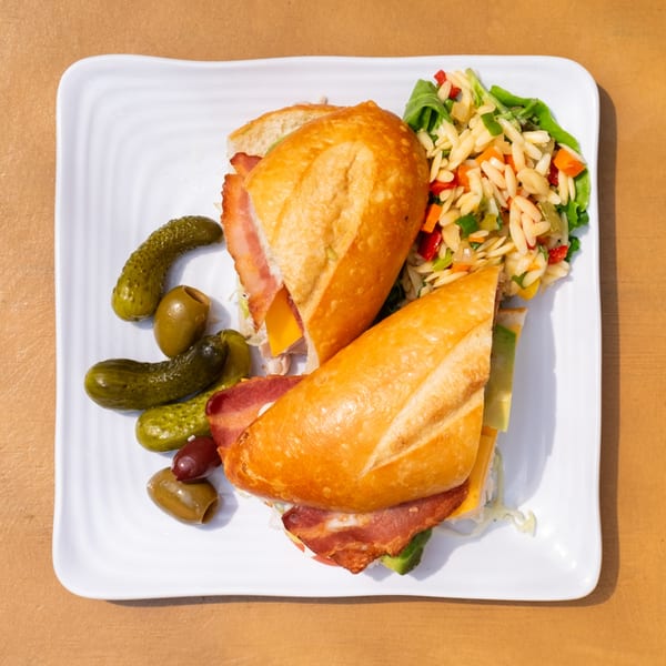 A Tardino Brother's Italian sandwich with bacon, cheese, and avocado, served with orzo salad and pickles.